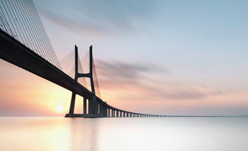 Calm water under a suspension bridge at dusk