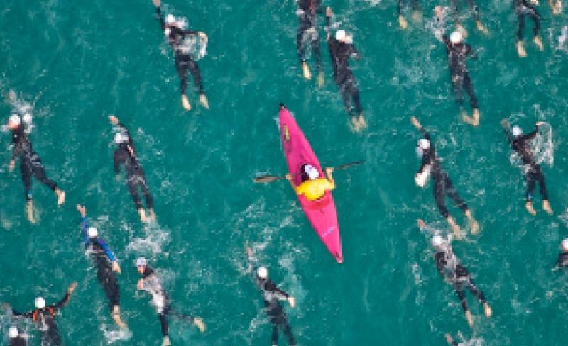 Person kayaking surrounded by a group of swimmers